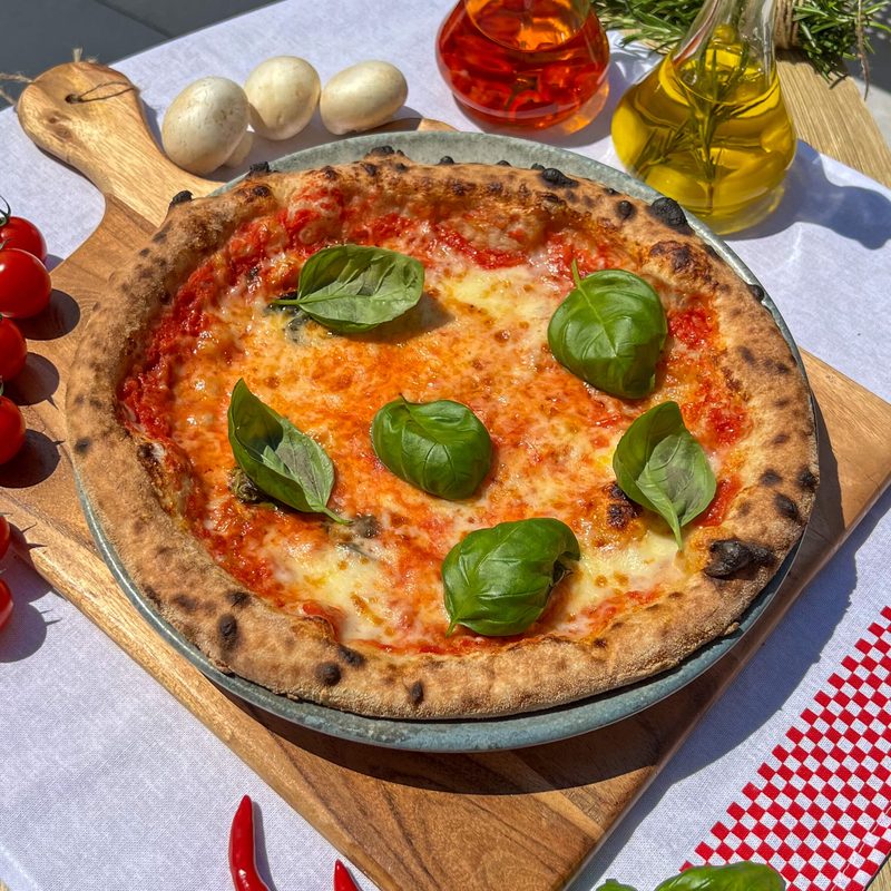 Pizza Margherita z mozzarellą fior di latte i listkami bazylii na drewnianej desce
