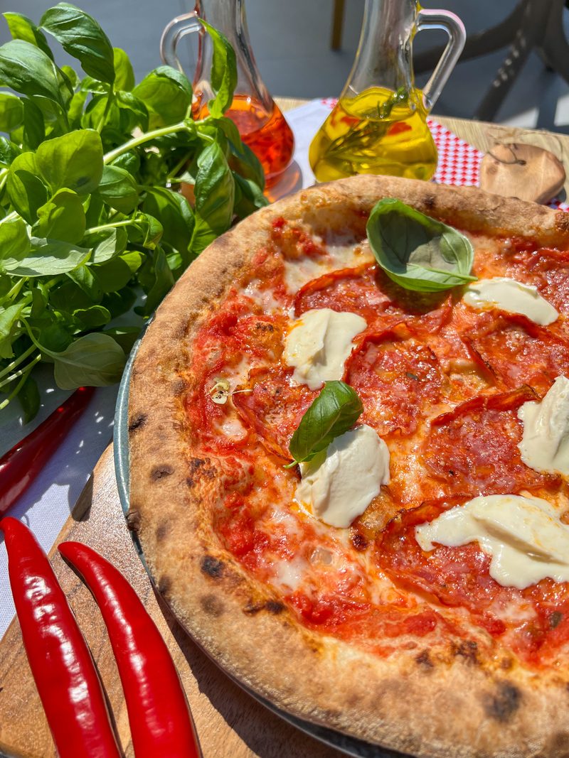 Pizza Salami Picante z pikantnym salami i mascarpone, obok pęk świeżej bazylii i oliwa z oliwek